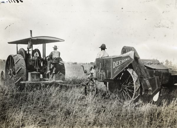 Two men working in a field: one operating an International tractor, and the other operating a Deering harvester-thresher(?) (combine?). The machine appears to be experimental.