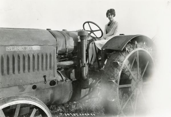 Marjorie Holsteen sits on top of a McCormick-Deering 15-30(?) tractor wearing a light dress and stockings.