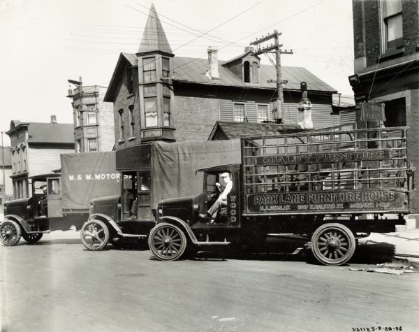 Three International Model 63 trucks parked in a street with their drivers. One truck has a canvas-covered bed and the text: "M.&M. Motor Service" printed on the side. Another has the text "Quality Furniture: Park Lane Furniture House" printed on the side.