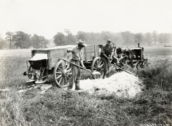 Two men using a Farmall Regular tractor, a farm wagon, and a lime spreader to spread lime in a field.