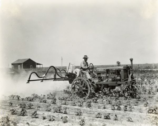 A man is using a Farmall Regular tractor with a spraying attachment to apply pesticide(?) to a crop.
