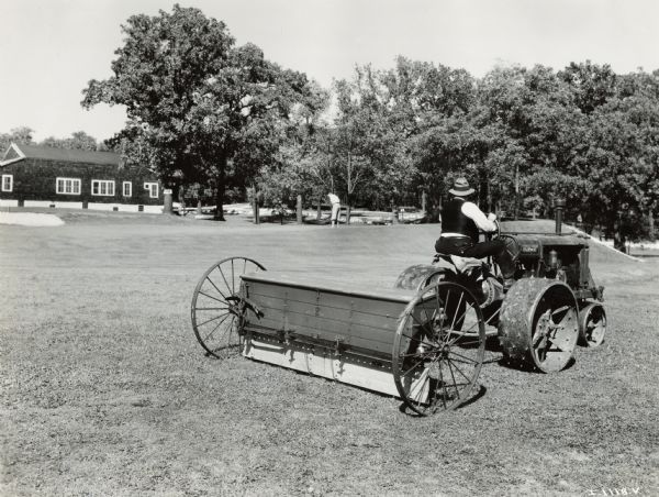 A groundskeeper at Indian Head Golf Club uses a McCormick-Deering Fairway tractor and seeder(?) to maintain the golf course. A man playing golf is in the background.