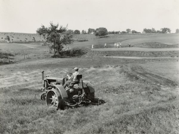 A groundskeeper uses a Fairway tractor to care for the rough of the Monroe Country Club golf course while a group of golfers plays in the background.
