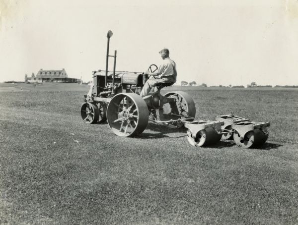 A groundskeeper uses a Farmall (or Fairway?) tractor with a roller  to tend the golf course at Aurora Country Club.