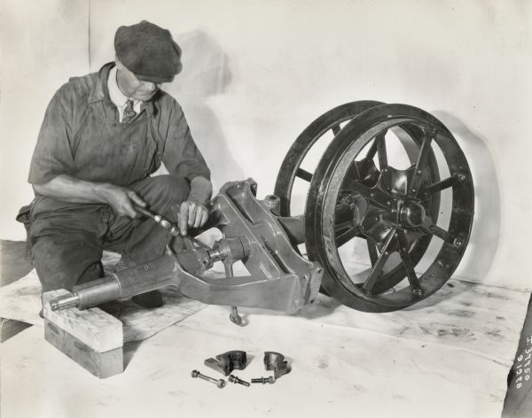 A man is using a hammer on the front wheel assembly of a Farmall Regular tractor.