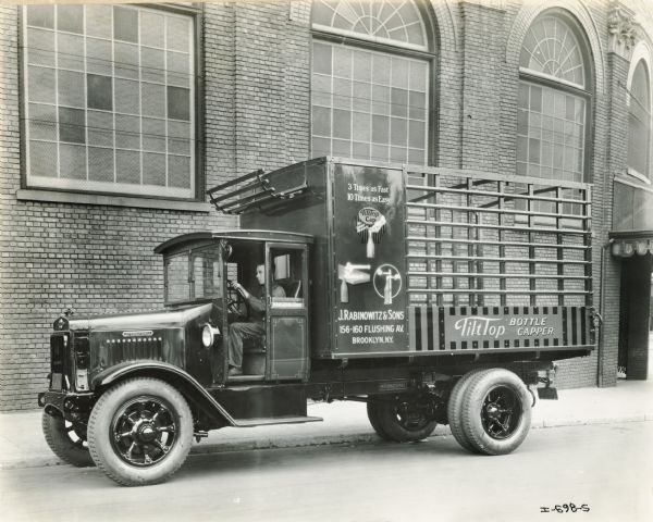 A driver is sitting in an International truck operated by J. Rabinowitz and Sons, purveyors of the "TiltTop Bottle Capper." Text on the truck reads: "3 times as fast, 10 times as easy; J. Rabinowitz & Sons; 156-160 Flushing Av. Brooklyn, N.Y.; TiltTop Bottle Capper."