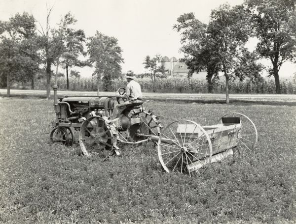 Man pulling a McCormick-Deering lime spreader with a Farmall Regular tractor. A barn and silo are in the background.