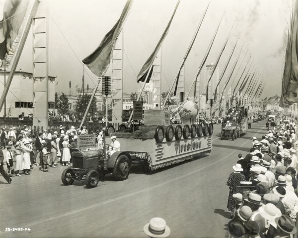 A group of spectators at the "A Century of Progress" world's fair watch an International Harvester tractor pull a Firestone float down the "Avenue of Flags" during the "Automotive Week Parade."