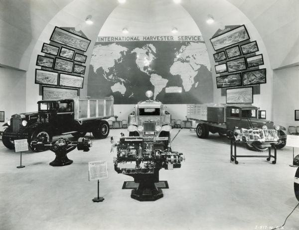 Interior of the International Harvester exhibit at the "A Century of Progress" world's fair. A world map, engine components, and trucks are on display.