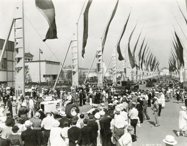 A woman driving an International Harvester tractor leads the Automotive Week parade down the "Avenue of Flags" at the "A Century of Progress" world's fair.