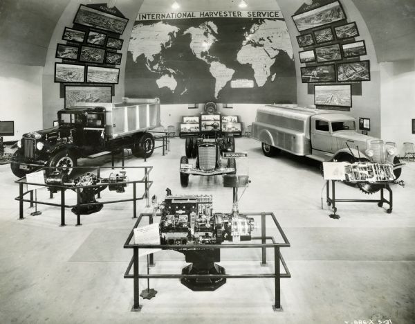 Interior of the International Harvester exhibit at the "A Century of Progress" world's fair. A world map, engine components, and trucks are on display.