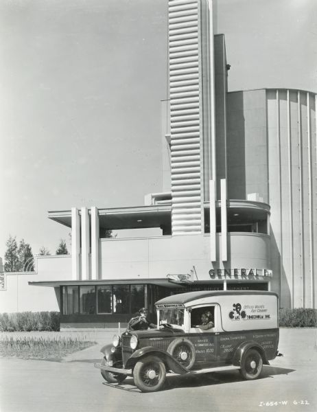 A man with garment bags over his shoulder leans against an International truck at the "A Century of Progress" world's fair in Chicago. The truck was operated by the Carl Stockholm Co., the "Official World's Fair Cleaner."