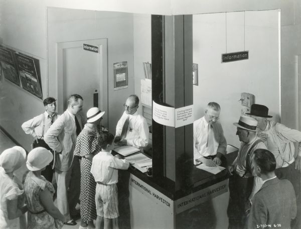 People standing around the International Harvester information and registration booth at the "A Century of Progress" world's fair. The sign attached to the post reads: "Visiting dealers, distributors, and Harvester men please register here."