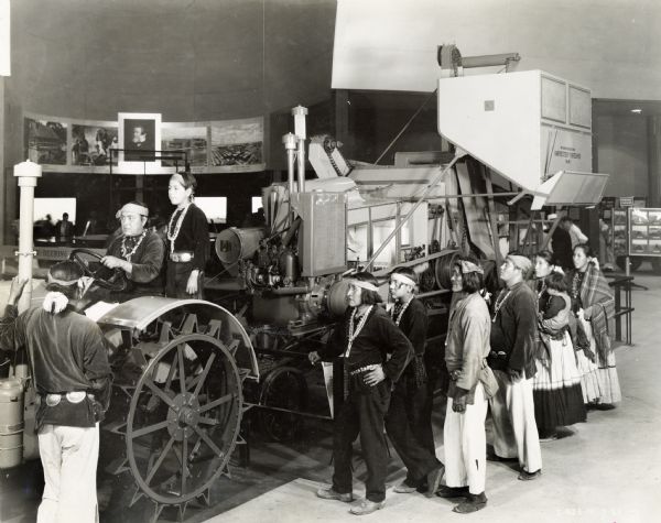 Native Americans in traditional dress test a harvester-thresher (combine) in the International Harvester exhibit at the "A Century of Progress" world's fair.