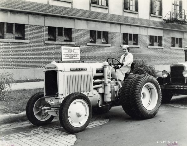 A woman is sitting on a tractor for the "A Century of Progress" world's fair, possibly in preparation for the Automotive Week parade.