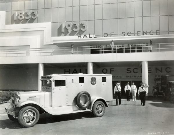 Uniformed men (Brinks staff?) standing beside an International Model B-3 truck parked outside the Hall of Science at the "A Century of Progress" world's fair. The truck appears to be a Brinks armored vehicle.