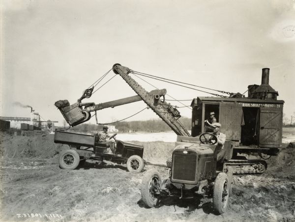 A shovel, or excavator loads dirt into an International Model S truck. The text on the wooden cab of the shovel appears to read: "Marion Shovel - Model 21".