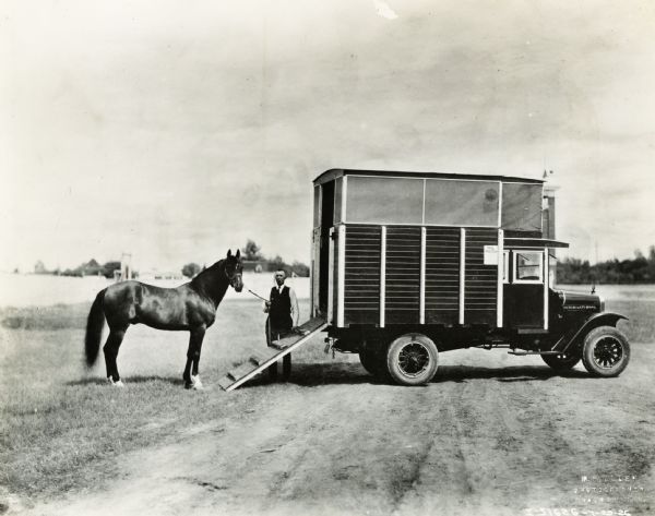 A man holding a horse by the reins stands at the back of an International Model S truck. On a small sign on the side of the truck bears the words "PHL Patch".