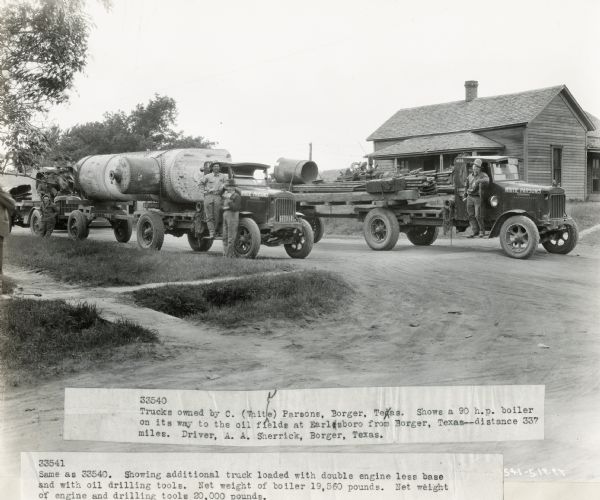 International Model 63 trucks parked on a dirt street. According to the original caption, the trucks were owned by C. Whitie Parsons, of Borger, Texas. The truck on the left carried a 90 h.p. boiler on its way to the oil fields at Earlsboro from Borger--a distance of 337 miles. The driver of this truck was A.A. Sherrick of Borger. The second truck, on the right, is loaded with "double engine less base" and oil drilling tools. The net weight of the boiler was 19,560 pounds. The net weight of the engine and drilling tools was 20,000 pounds.