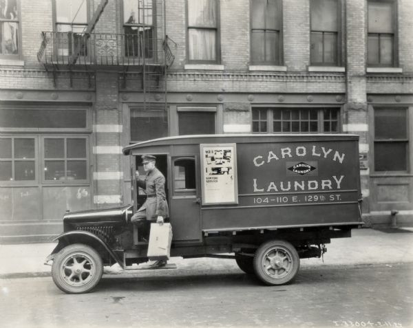 A uniformed worker holding a package steps out of an International Model S truck operated by the Carolyn Laundry.