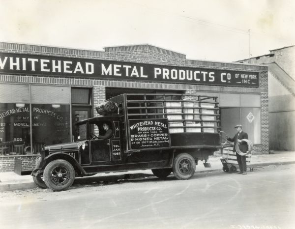 A man loading an International Model S truck in front of the Whitehead Metal Products Company building.