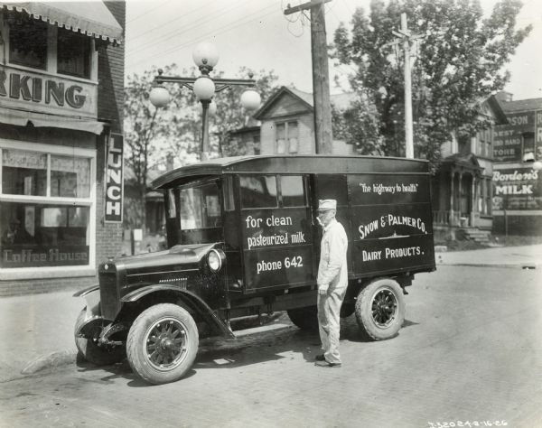 A man stands outside an International Model S truck used to deliver Snow & Palmer dairy products. Text on the truck reads: "for clean, pasteurized milk" and "the highway to health".