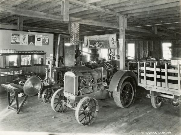 A McCormick-Deering 10-20(?) tractor, a Farmall Regular tractor with a saw attached, and other agricultural equipment on display in the showroom of an International Harvester dealership, possibly the Evans Implement Company. Several advertising posters are hanging on the wall.
