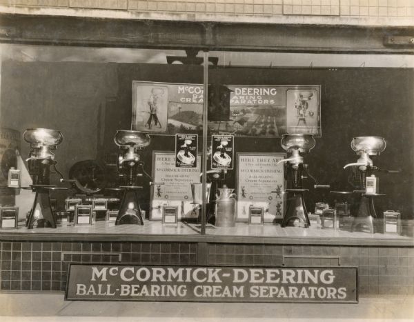 New ball-bearing cream separators on display in the storefront window of the Burlington Farm Machinery Company, an International Harvester dealership. The posters in the display read: "Here They Are: A New and Complete Line of McCormick-Deering Ball-Bearing Cream Separators; Built in Six Sizes; Hand, Electric, Power Driven. Ask for a Demonstration."