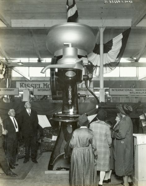 Men and women gather around a giant model of a cream separator, possibly at the Wisconsin State Fair.