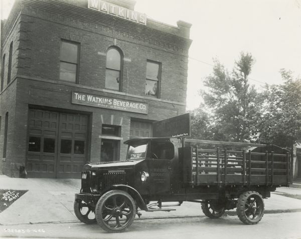 An International Model 63 truck parked ouside the Watkins Beverage Company building. A sign on the truck reads: "Gold Springs Ginger Ale; Every Swallow Pure."