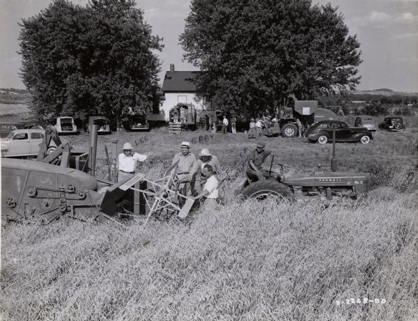 Lee and Gray, International Harvester employees, and Fowler McCormick, looking at an experimental combine (harvester-thresher) in a field. A Farmall tractor is nearby. The original caption reads: "International Harvester engineers and officials are studying the performance of an experimental harvester-thresher, or combine, on a mid-western farm. Harvester machines are never put into commercial production until experimental and "preproduction" models have been exhaustively tested in actual farm operation. This machine is part of the Harvester "caravan" which follows the harvest from south to north."