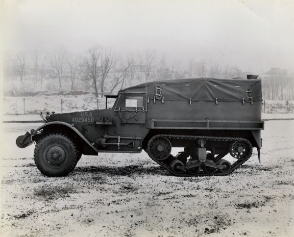 A military half-track redesigned and improved by International Harvester automotive engineers parked in the snow. The original caption reads: "At the Army's request International Harvester automotive engineers redesigned and improved the military half-track. International Harvester engineers also devised the first successful method of bending and welding homogeneous armor plate, thus making these combat vehicles safer for their occupants while under enemy fire." The vehicle is marked U.S.A. 4029450.