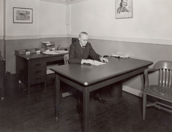 C.R. Rogers, chief engineer of International Harvester Company's Gas Power Engineering Department, sitting behind a desk. The original caption reads: "C.R. Rogers, chief engineer of International Harvester Company's Gas Power Engineering Department, at Chicago, looks over the report of results obtained during tests of an experimental model of a farm tractor."