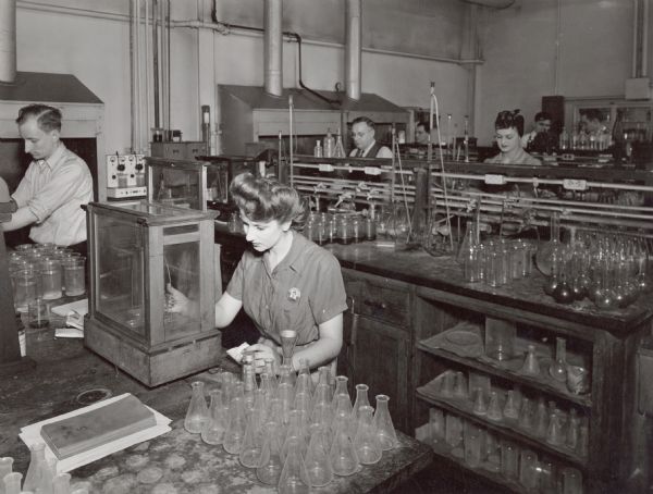 Gertrude Satina weighs a piece of steel in the chemical laboratory at the International Harvester Company. The original caption reads: "This photo shows the chemical laboratory at Gas Power Engineering Department of International Harvester Company, at Chicago. Miss Gertrude Satina is weighing a sample of steel which is under chemical test."