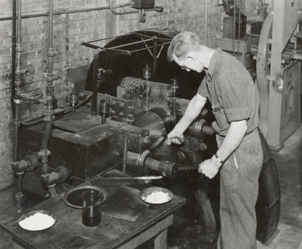 Arnold Batson works with natural and synthetic rubbers in the rubber laboratory at the Gas Power Engineering Department. The original caption reads: "Experiments with natural and synthetic rubbers are carried on in the rubber laboratory at International Harvester's Gas Power Engineering Department, at Chicago. Various formulas are devised and tested to get the right rubber compound for each need. Arnold Batson is compounding a new batch at rubber mill."