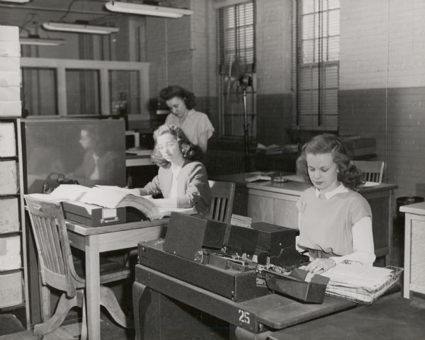 Three women are performing secretarial work in an office at International Harvester's Tractor Works.
