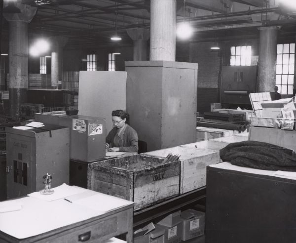 A woman is sitting behind a desk in an office at International Harvester's Tractor Works.