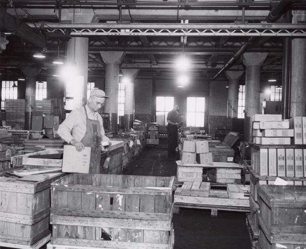 Two factory workers are loading boxes into crates at International Harvester's Tractor Works.
