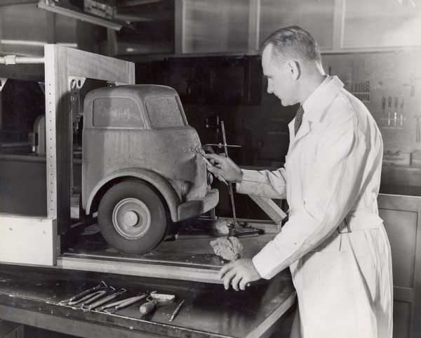Jack Gordon uses a tool to shape a clay model truck in the truck engineering department. The original caption reads: "Truck stylist Jack Gordon works on a quarter-size clay model of a cab-over-engine motor truck in the International Harvester truck engineering department at Fort Wayne, Ind. Other models are made of wood. Styling is a factor of increasing importance in truck designing."