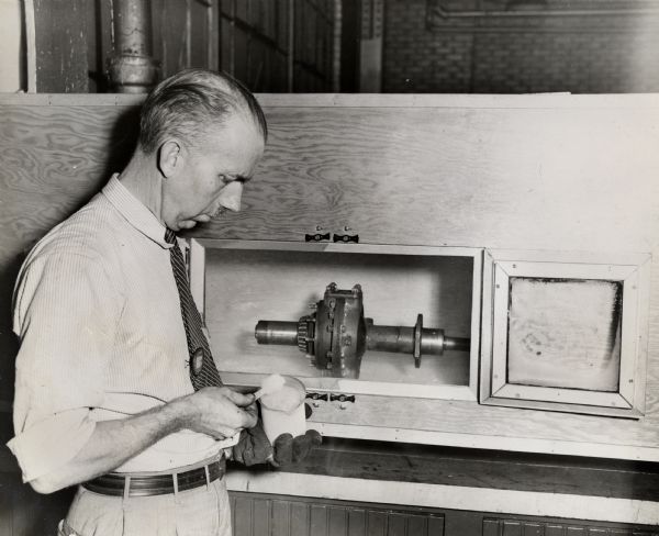 Jerry Moreland tests a front drive joint assembly in a freezing cabinet at the International Harvester truck engineering department. The original caption reads: "The substance Jerry Moreland is dipping from the beaker is kerosene, which has been taken from the freezing cabinet in which a front drive joint assembly is being tested in a temperature of 60 degrees below zero. The Harvester truck engineering department at Fort Wayne also has a heat cabinet in which operational tests are made in temperatures up to 400 degrees above zero."