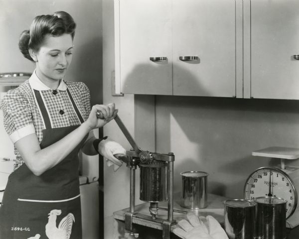 A woman wearing an apron using a counter-mounted can opener.