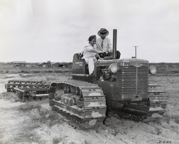 Wesley Kolkhorst shows Lillian A. Heinrichs how to operate a TracTracTor (crawler tractor). The original caption reads: "Mrs. Lillian A. Heinrichs learns the intricacies of TracTracTor operation from Wesley Kolkhorst, salesman and part time instructor for Mr. August Eltiste's Santa Ana, California dealership." The instruction was likely part of International Harvester's "Tractorette" program.