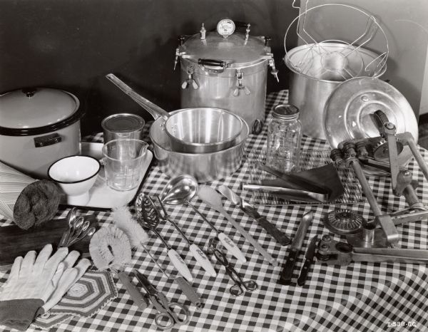 An assortment of kitchen pots, pans, and utensils spread out on a checkered tablecloth.