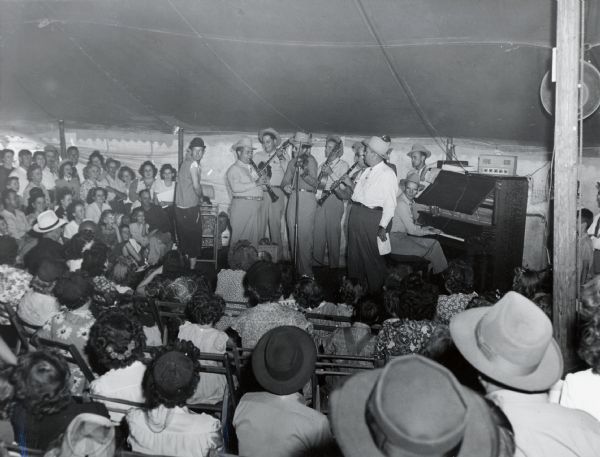 An audience watching a musical group put on a show in a tent at the Kansas State Fair.