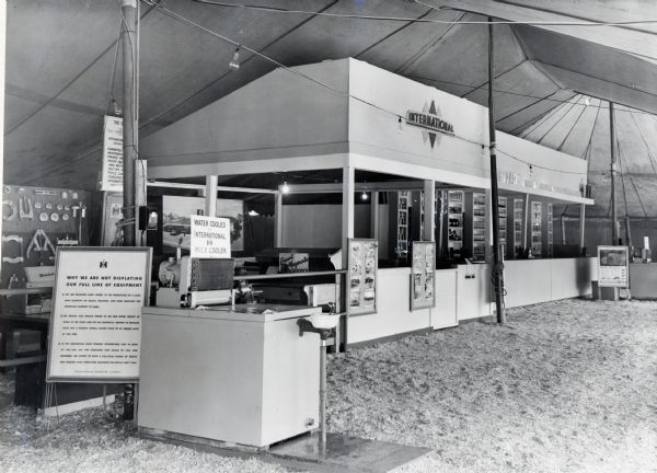 A drinking fountain "Cooled by International Milk Cooler" stands in front of the International Harvester booth at the Texas State Fair. The title on the sign in the foreground reads: "Why We Are Not Displaying Our Full Line of Equipment."
