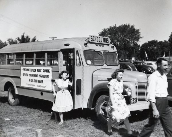 Several people get off a school bus used to transport fairgoers from downtown Des Moines to the Iowa State Fair. The sign on the side of the bus reads: 'First Iowa Television Public Showing; See - Hear Popular KRNT Personalities in Our Tent Theater; International Headquarters."