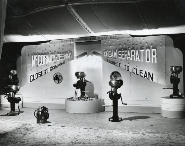 Cream separators stand on display against a backdrop at the Dairy Cattle Congress. The display text reads: "Newest Star in the Milky Way; McCormick-Deering Cream Separator; Closest Skimming, Easiest To Clean."