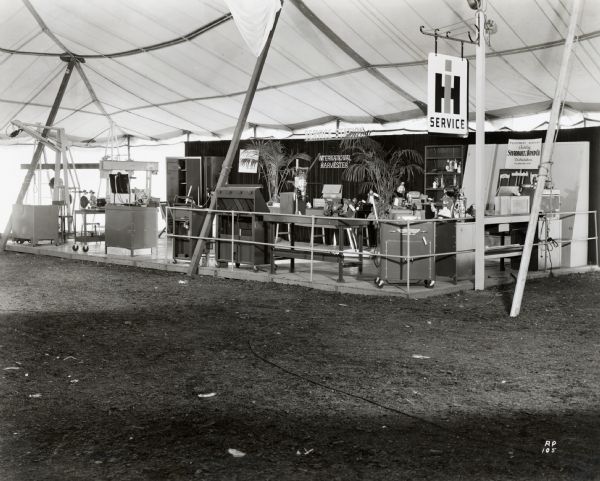 International Harvester Company displays its products under a tent at the Wisconsin State Fair. The text on the sign reads: "Equipment Display Courtesy Shadbolt & Boyd Co., Distributors, Milwaukee, Wis."