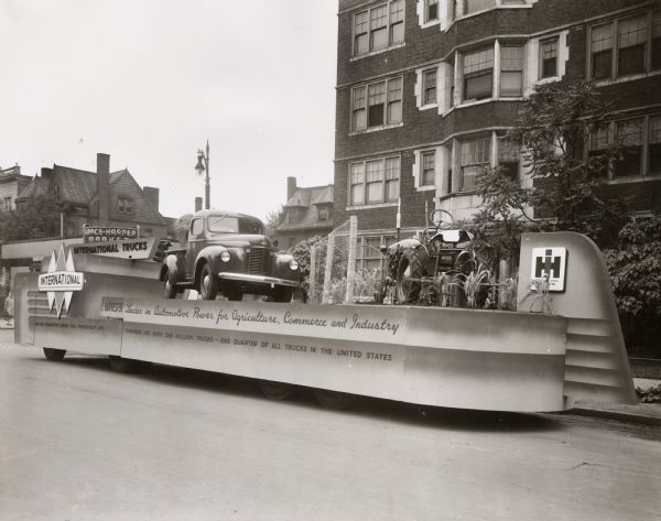 An International Harvester parade float in the Golden Jubilee celebration parked alongside a road. The text on the side of the float reads: "Motor Transport Serves You Throughout Life," "Harvester: Leader in Automotive Power for Agriculture, Commerce and Industry," and "Farmers Use Over One Million Trucks -- One Quarter of All Trucks in the United States."