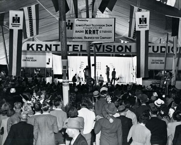 A crowd gathers to watch "Iowa's First Television Show" at the Iowa State Fair International Harvester headquarters. The sign hanging above the audience reads: "Presenting Iowa's First Television Show in Cooperation With Radio KRNT Studios, International Harvester Company."